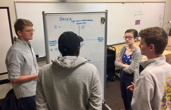 Undergraduate student members of the STS Futures Lab stand at a whiteboard as they collaborate on a scenario analysis related to implementation precision medicine